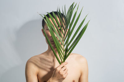 Shirtless man holding leaves against white background
