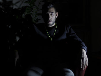 Portrait of young man sitting on chair in darkroom at night