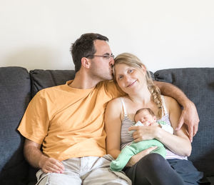 Husband kissing wife with son sitting on sofa