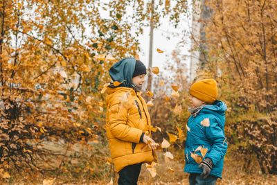 Boys in a jacket scatter leaves in an autumn park. the child rejoices in the autumn leaves.