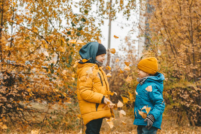 Boys in a jacket scatter leaves in an autumn park. the child rejoices in the autumn leaves.