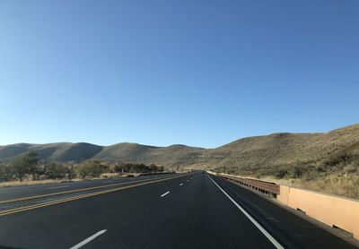 Road leading towards mountains against clear blue sky