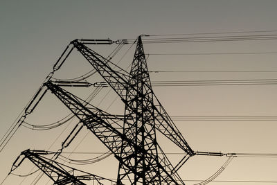 Low angle view of silhouette electricity pylon against clear sky