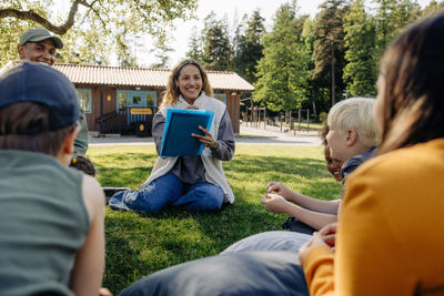 Smiling camp counselors doing activities with children while sitting on grass at summer camp