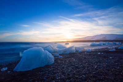 Ice at beach against sky during sunset