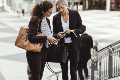 Businesswoman showing smart phone to female colleague while standing outdoors