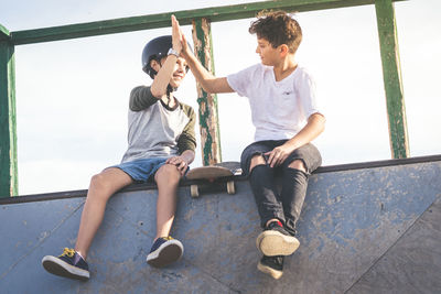 Boy giving high-five to friend while sitting on retaining wall