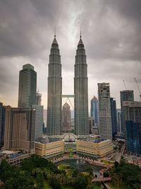 Petronas towers and buildings against cloudy sky