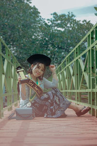 Full length of woman sitting on bridge against plants