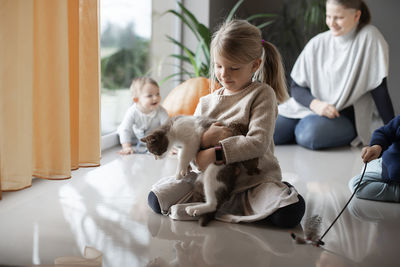 Mother with her three children playing with a cat on the floor at home