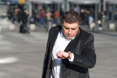 Man checking time on wristwatch while standing in city