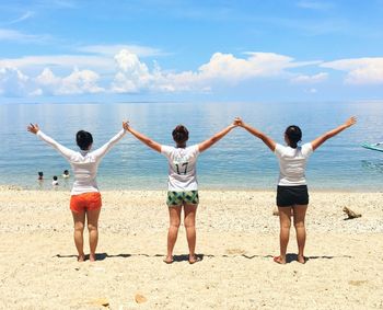 Rear view of friends standing on beach against sky