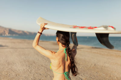Rear view of woman carrying surfboard while walking at beach