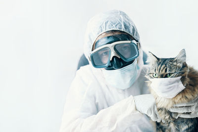 Woman in biohazard suit holding cat against white background