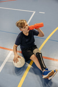 High angle view of male athlete drinking water after football match at sports court