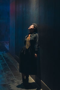 Woman looking away while standing against wall