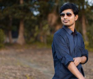 Young man wearing sunglasses while standing against trees