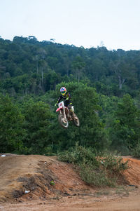 Man performing stunt with motorbike against trees