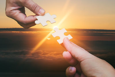 Midsection of person holding sun against sky during sunset