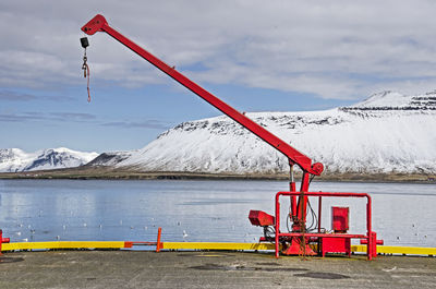 Small harbour crane, painted bright red, with snow-covered mountains in the background