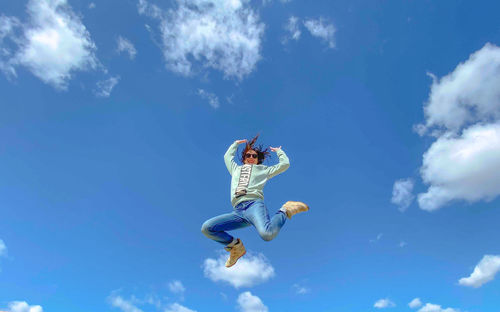 Low angle view of person jumping against sky