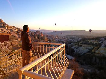 Rear view of man looking at hot air balloons against sky during sunset