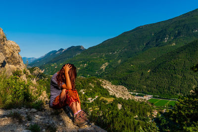 Man sitting on mountain against sky