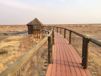 Wooden boardwalk on field against clear sky