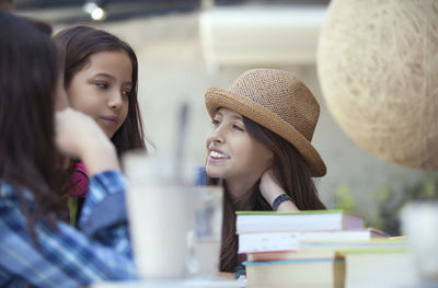 Smiling girl looking at friends while sitting by books on desk