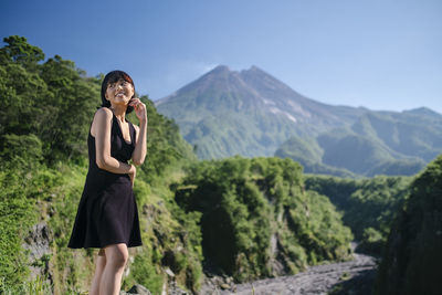 Smiling young woman standing on land against mountains and sky