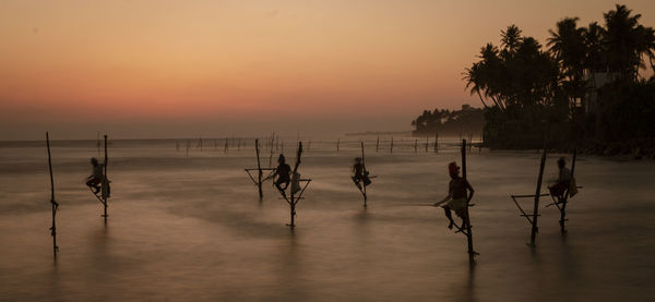 Silhouette people on beach against sky during sunset