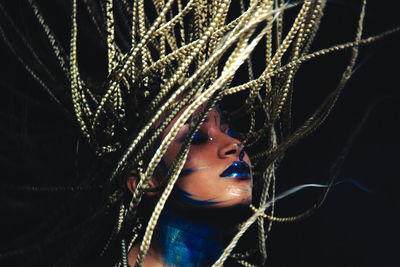 Close-up of woman with face paint and tousled braided hair against black background