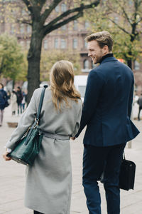 Rear view of businesswoman with handbag walking by colleague in city