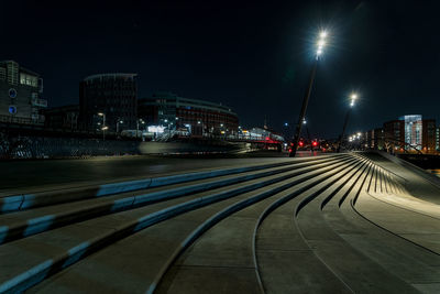 Illuminated street amidst buildings against sky at night