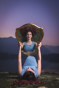 Woman holding mirror with her reflection against mountains