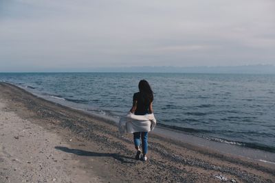 Rear view of woman on beach against sky