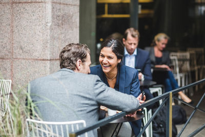 Happy businesswoman sitting with coworker at sidewalk cafe