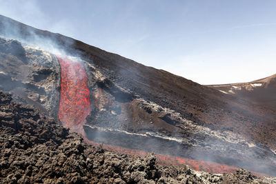 Glowing lava flow flowing on etna volcano in sicily , with smoke and lava flow channel 7 june 2022