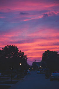 Silhouette trees by road against dramatic sky