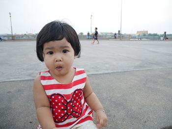 Portrait of cute girl sitting on street against clear sky