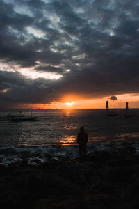 Silhouette people on beach against sky during sunset