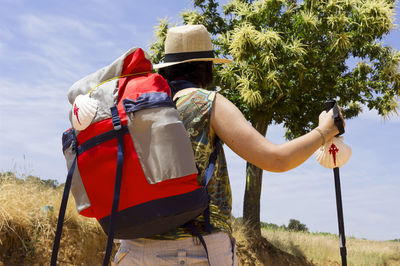 Low angle view of hiker in hat with backpack walking against sky during sunny day