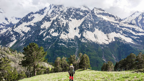 Rear view of person walking on snowcapped mountains against sky