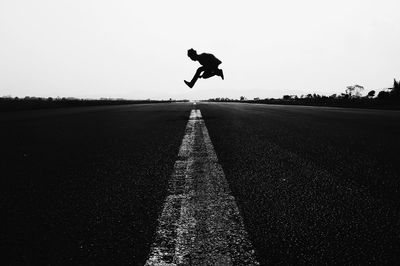 Man jumping on road against sky