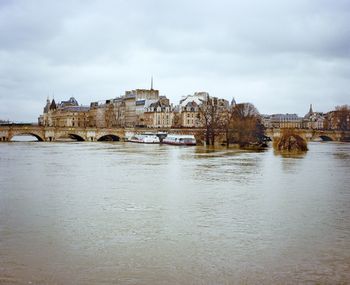 Bridge over river in city against cloudy sky