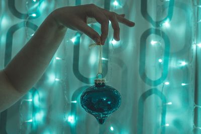 Cropped hand of woman holding christmas decoration against illuminated lights