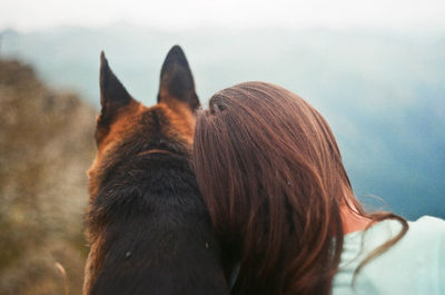 Rear view of young woman with dog sitting on mountain against sky