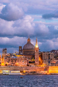 View of illuminated buildings in valletta against cloudy sky