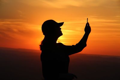 Silhouette woman standing against orange sky during sunset