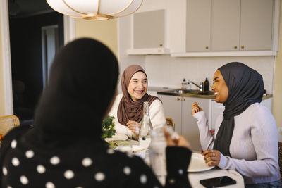 Happy young women in hijabs having dinner together at home